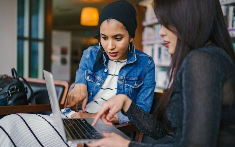 two women looking and pointing at macbook laptop